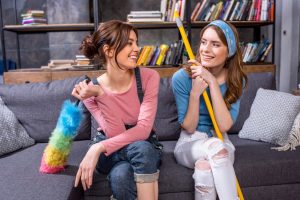 TWo friends with cleaning mops sitting on sofa laughing
